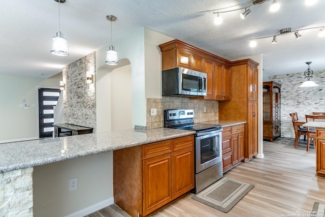 kitchen featuring brown cabinetry, hanging light fixtures, light wood finished floors, backsplash, and stainless steel appliances