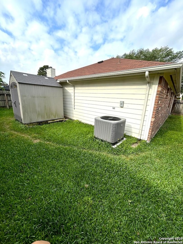 rear view of property with central air condition unit, a storage shed, an outdoor structure, brick siding, and a lawn