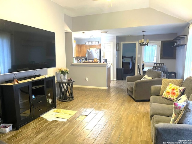 living area with vaulted ceiling, light wood-type flooring, a chandelier, and baseboards