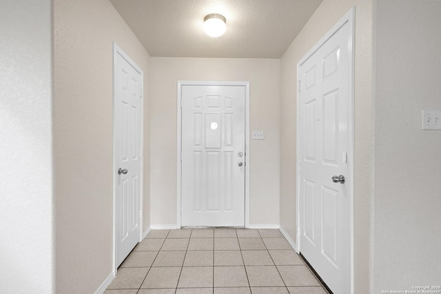 doorway to outside with light tile patterned flooring, a textured ceiling, and baseboards