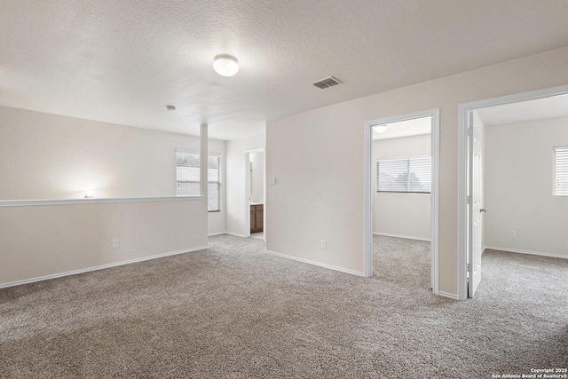 spare room featuring carpet, a wealth of natural light, visible vents, and a textured ceiling