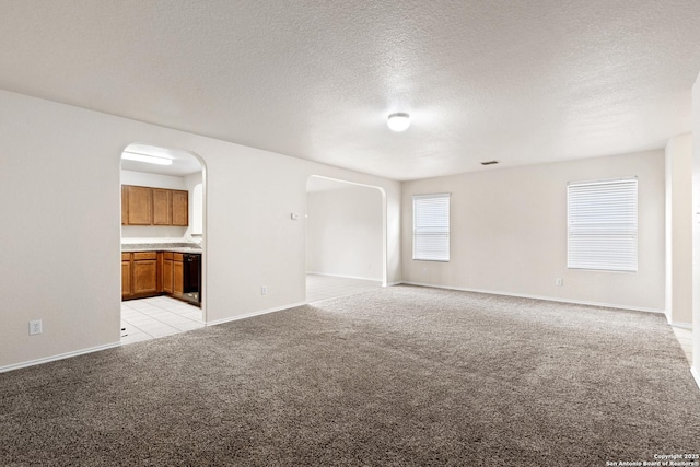 unfurnished living room featuring arched walkways, light carpet, a textured ceiling, and baseboards