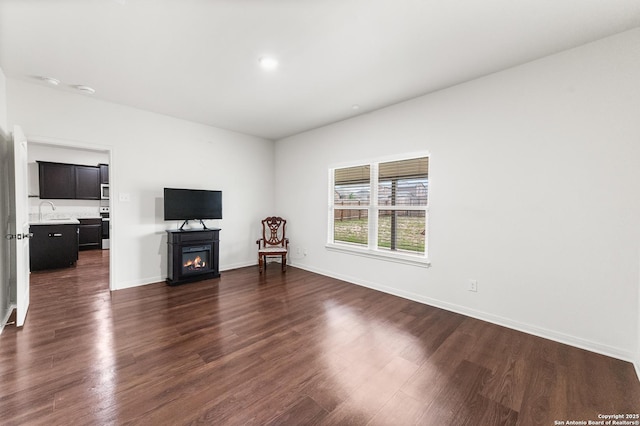 15102 Jetfire, Von Ormy, TX 78073 - unfurnished living room featuring baseboards, a warm lit fireplace, a sink, and dark wood-type flooring