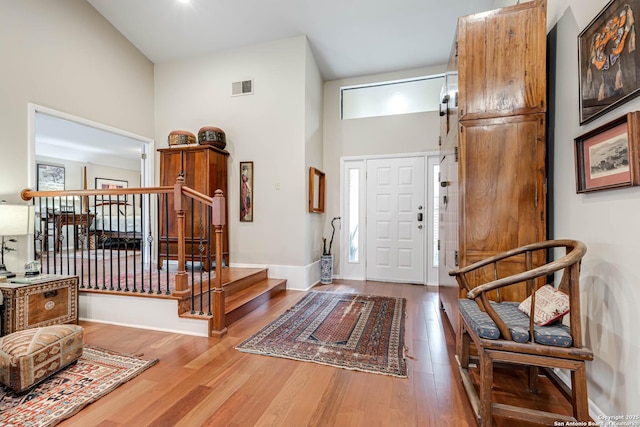 entrance foyer featuring stairs, wood finished floors, visible vents, a high ceiling, and baseboards
