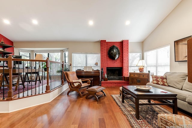 living room featuring high vaulted ceiling, wood finished floors, a brick fireplace, and recessed lighting