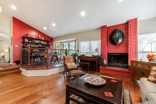 living area featuring lofted ceiling, a brick fireplace, recessed lighting, and wood finished floors