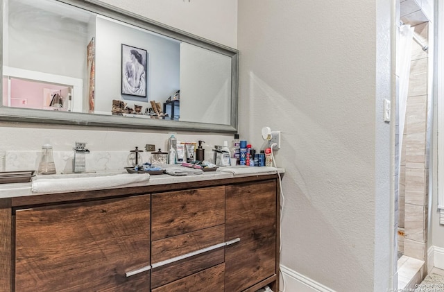full bathroom with walk in shower, baseboards, vanity, and a textured wall