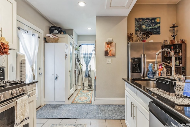 kitchen featuring light tile patterned flooring, a sink, dark countertops, stainless steel appliances, and white cabinets