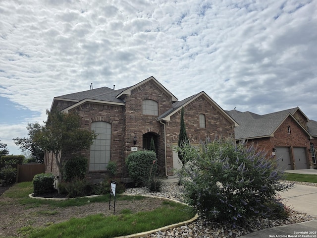 view of front of property featuring driveway, brick siding, a shingled roof, and fence