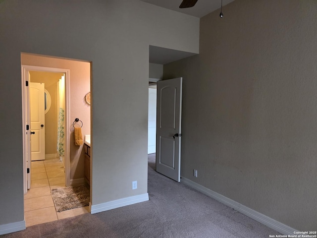 unfurnished bedroom with baseboards, ensuite bath, light tile patterned floors, and light colored carpet