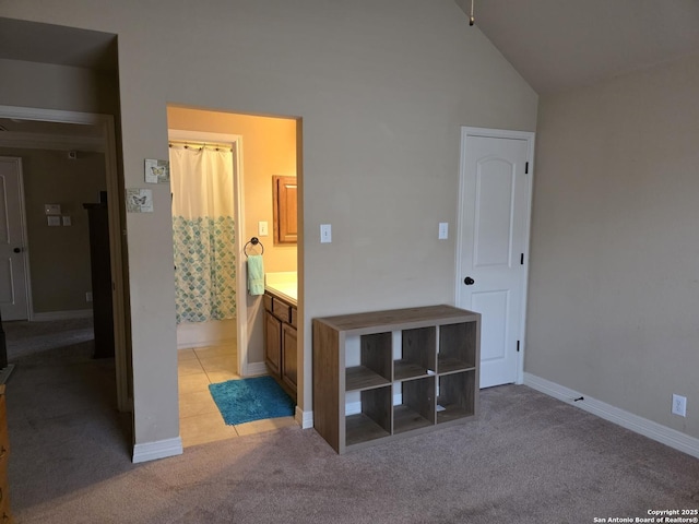 unfurnished bedroom featuring baseboards, light carpet, ensuite bath, and high vaulted ceiling