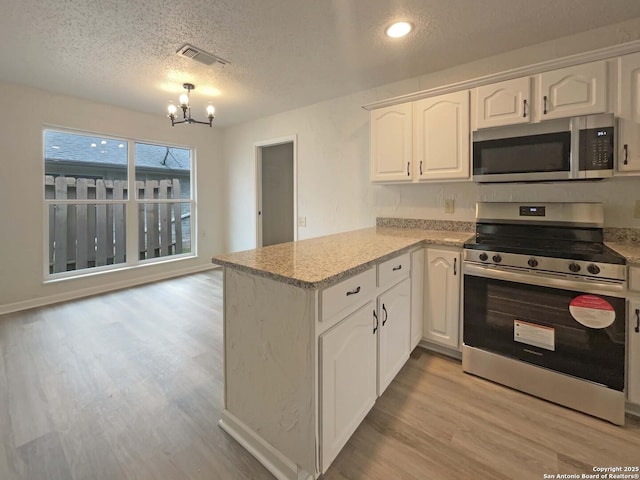 kitchen featuring appliances with stainless steel finishes, a peninsula, a textured ceiling, a chandelier, and white cabinetry