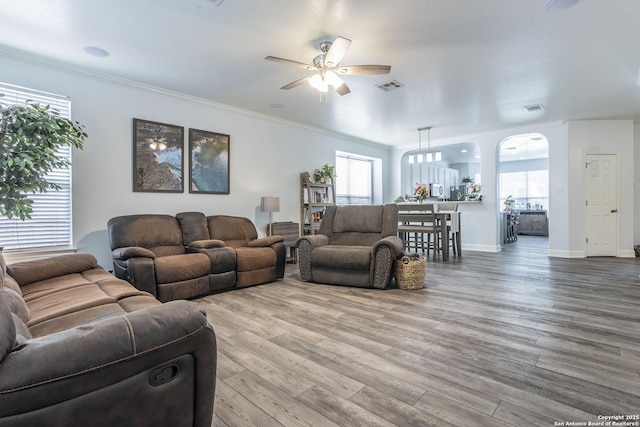 living area featuring a ceiling fan, wood finished floors, crown molding, and baseboards