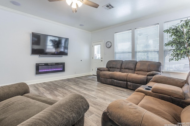 living room featuring a ceiling fan, healthy amount of natural light, crown molding, light wood-style floors, and a glass covered fireplace