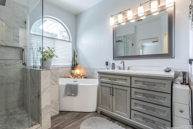 full bath featuring wood finished floors, a shower stall, vanity, a tub, and tile walls