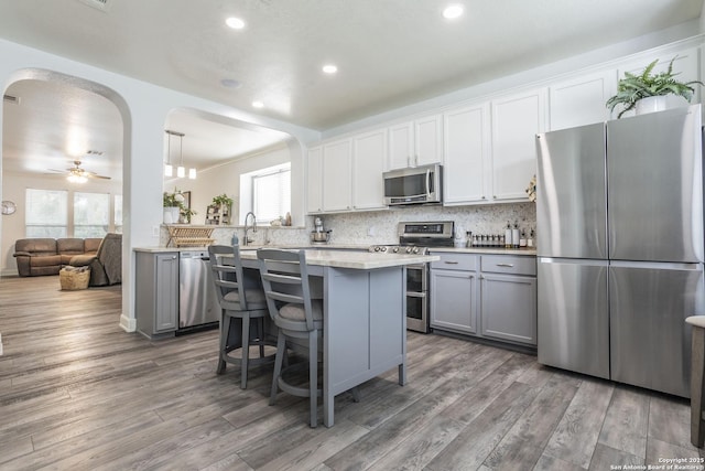kitchen with appliances with stainless steel finishes, arched walkways, wood finished floors, gray cabinets, and recessed lighting