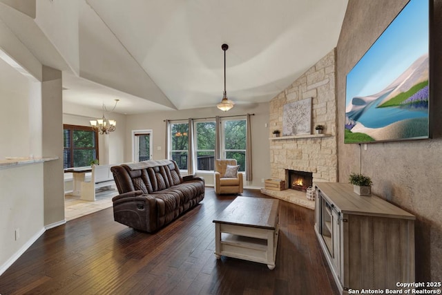 living area featuring vaulted ceiling, an inviting chandelier, a stone fireplace, and dark wood finished floors