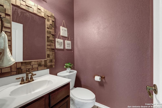 bathroom featuring toilet, baseboards, vanity, and a textured wall