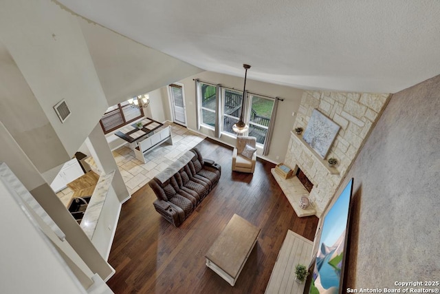 living room featuring lofted ceiling, a stone fireplace, an inviting chandelier, visible vents, and wood finished floors