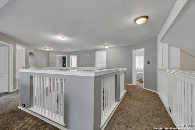 hallway with arched walkways, dark carpet, baseboards, and a textured ceiling