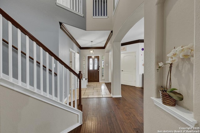 foyer entrance with hardwood / wood-style flooring, stairway, crown molding, arched walkways, and baseboards