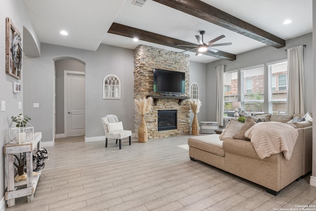 living room with a ceiling fan, arched walkways, light wood-style floors, a fireplace, and beam ceiling