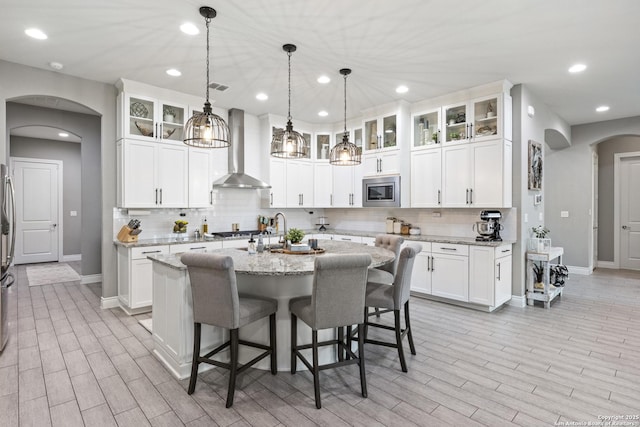 kitchen with wall chimney exhaust hood, stainless steel microwave, baseboards, arched walkways, and decorative backsplash