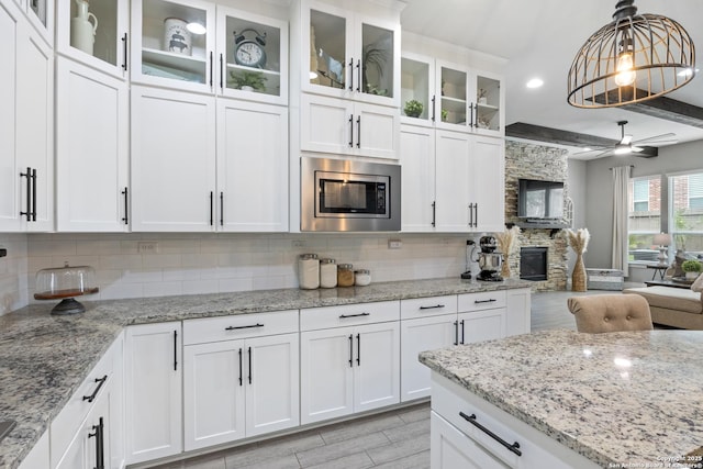 kitchen featuring stainless steel microwave, tasteful backsplash, decorative light fixtures, white cabinetry, and open floor plan