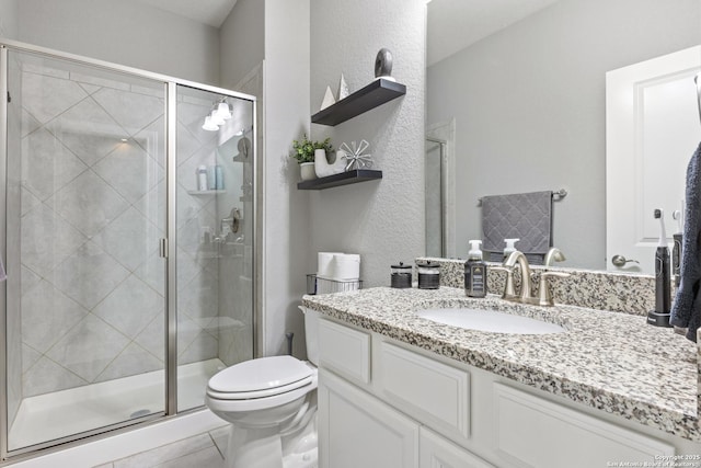 full bathroom featuring toilet, vanity, a textured wall, and a stall shower