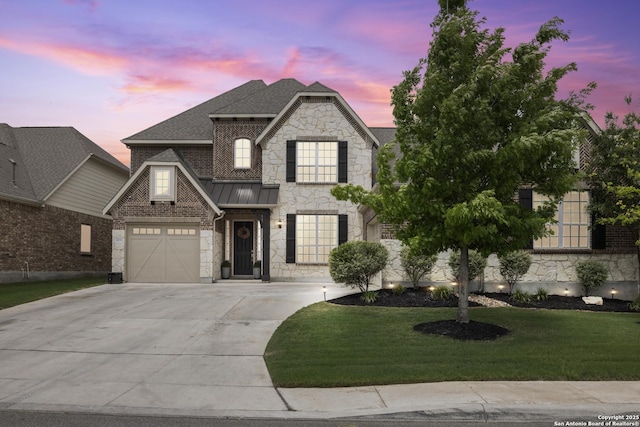 french country inspired facade with stone siding, concrete driveway, a front yard, a shingled roof, and a standing seam roof