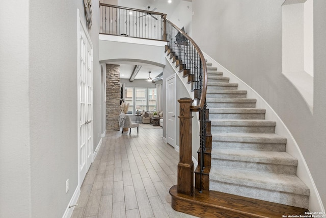 stairs featuring wood finished floors, arched walkways, a ceiling fan, a high ceiling, and baseboards