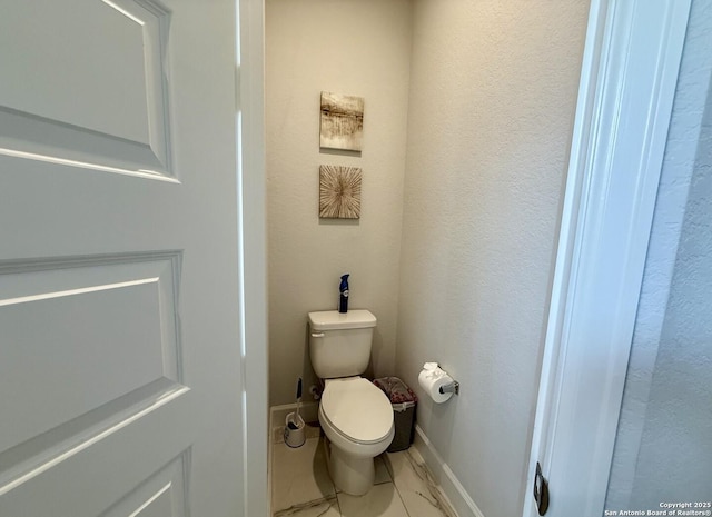 bathroom with toilet, baseboards, and marble finish floor