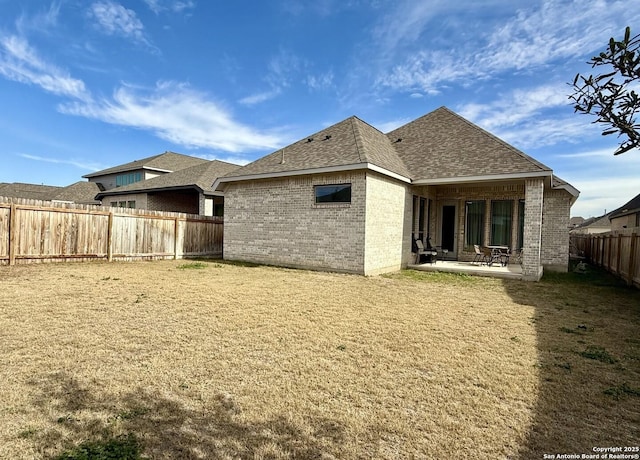 rear view of house with brick siding, roof with shingles, a fenced backyard, and a patio