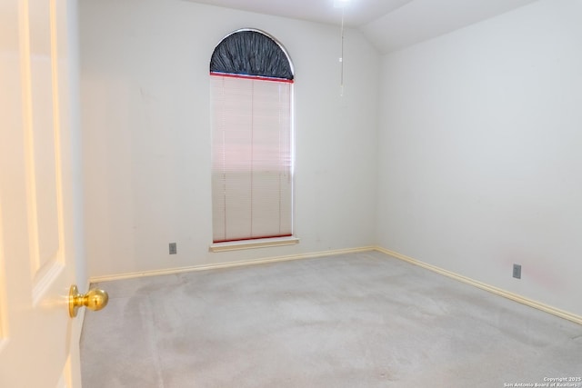 carpeted spare room featuring baseboards and lofted ceiling