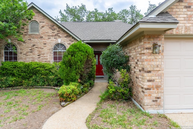 view of exterior entry with a shingled roof, brick siding, and an attached garage