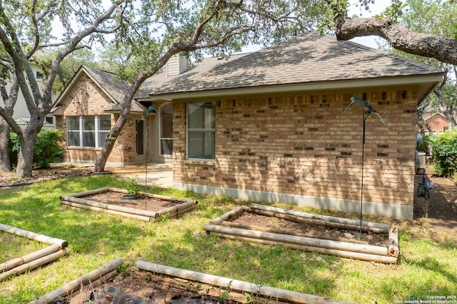 view of front of home with brick siding, a shingled roof, a chimney, and a garden