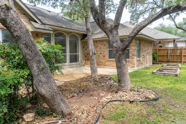 back of house with a shingled roof, a vegetable garden, brick siding, and fence
