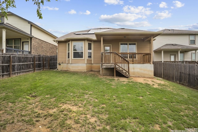 rear view of property with a lawn, a fenced backyard, and roof mounted solar panels