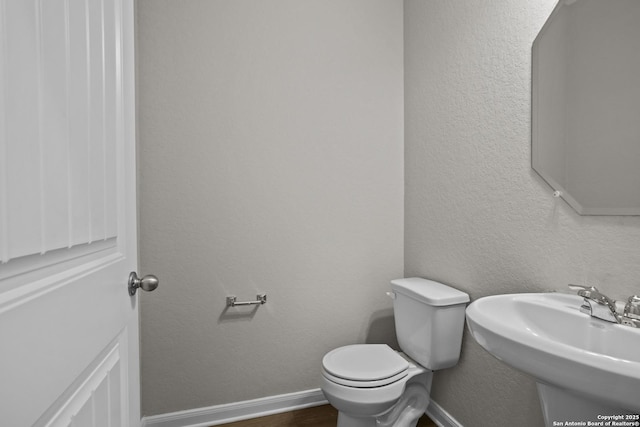 half bath with toilet, baseboards, a sink, and wood finished floors
