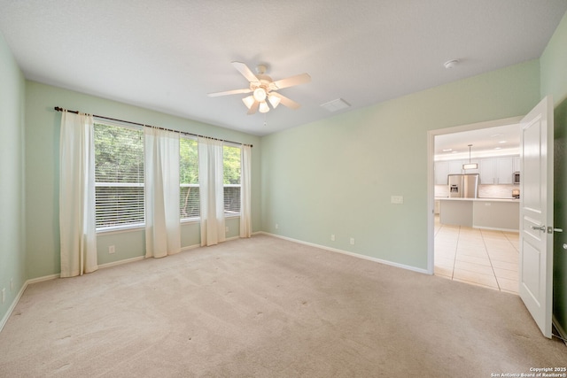 empty room featuring light colored carpet, baseboards, a ceiling fan, and visible vents