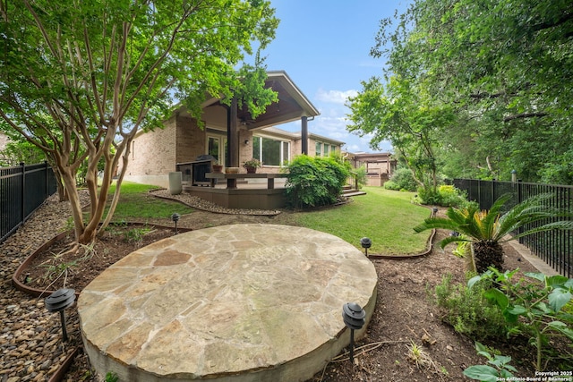 back of house featuring a yard, brick siding, a wooden deck, and a fenced backyard