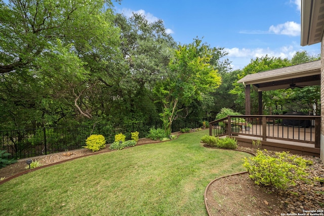view of yard with fence, a deck, and a ceiling fan