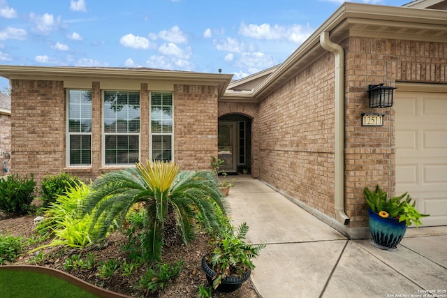 view of exterior entry featuring an attached garage and brick siding
