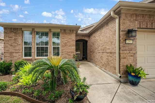 view of exterior entry featuring a garage and brick siding