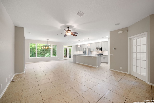unfurnished living room with ceiling fan with notable chandelier, baseboards, light tile patterned floors, and visible vents