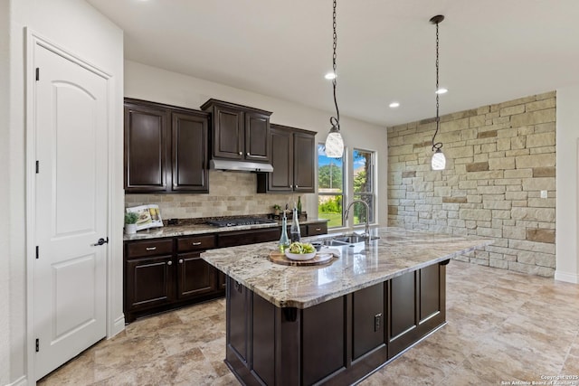 28546 Tristant Rdg, San Antonio, TX 78260 - kitchen featuring under cabinet range hood, light stone counters, hanging light fixtures, a sink, and gas stovetop