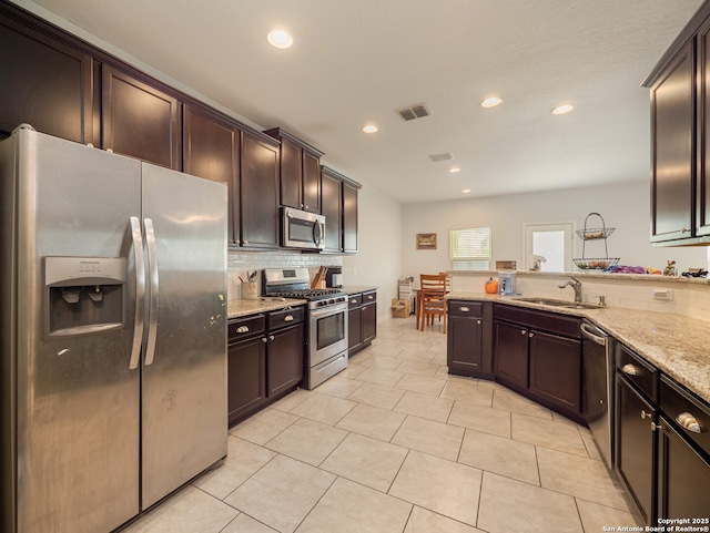 kitchen with backsplash, light stone counters, dark brown cabinets, and appliances with stainless steel finishes