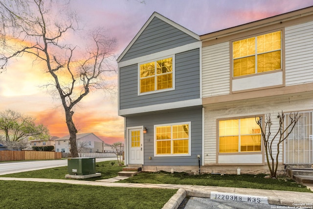back of property at dusk featuring a yard, fence, entry steps, and uncovered parking