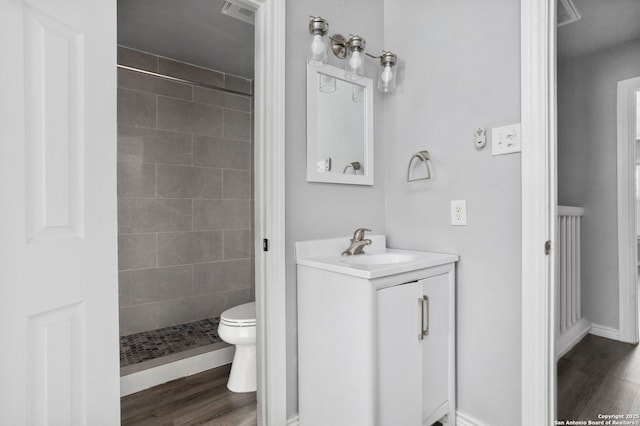 full bathroom featuring toilet, wood finished floors, vanity, visible vents, and tiled shower