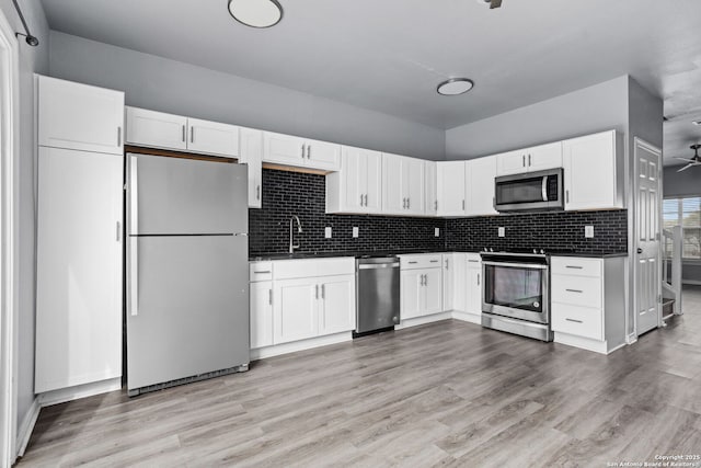 kitchen with dark countertops, stainless steel appliances, white cabinets, and light wood-style flooring